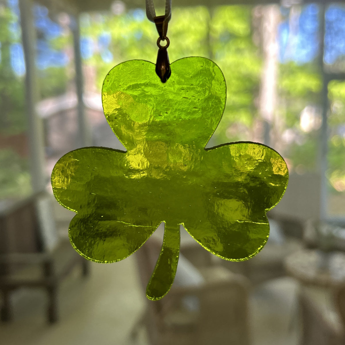 Stained glass shamrock hanging in a window with the light shining though.