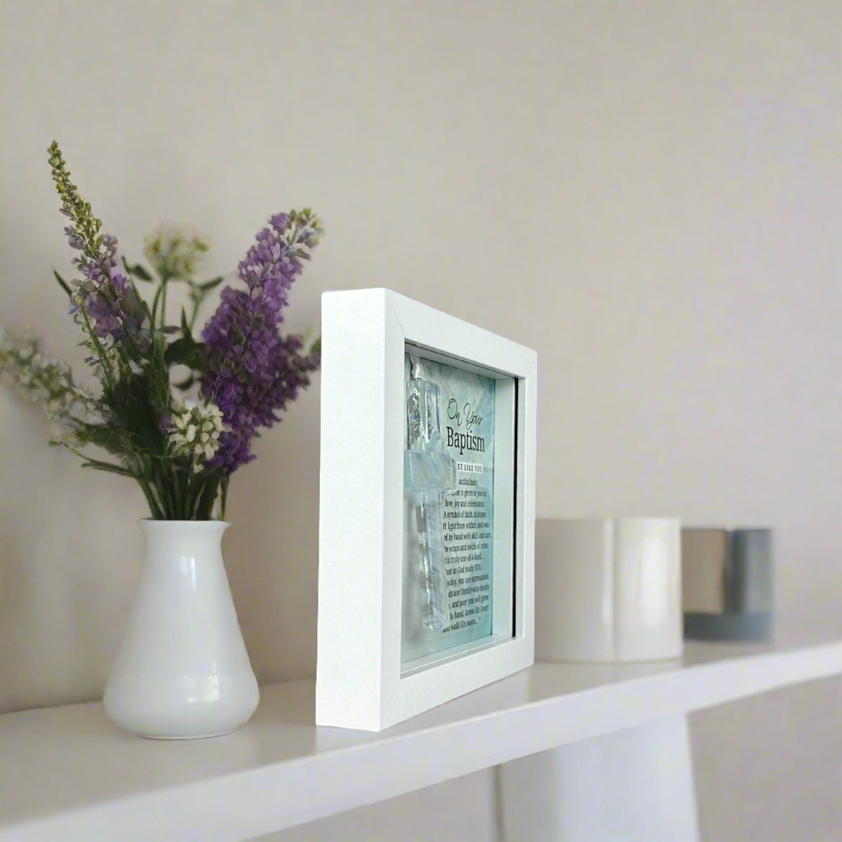 Framed Baptism cross on a bookshelf.