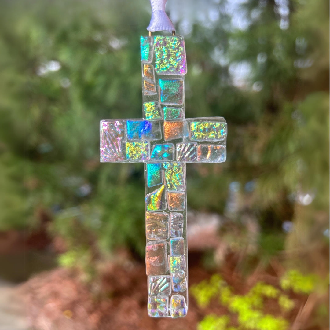 Dichroic Glass Cross hanging in a window showing the color variation caused by shining light.