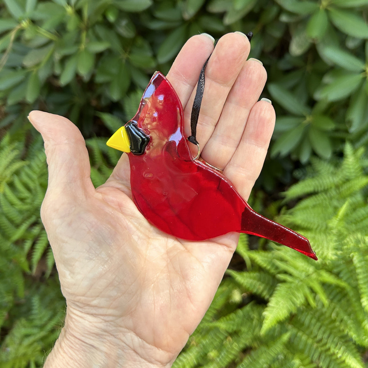 Handmade red stained glass cardinal ornament being held in a hand.