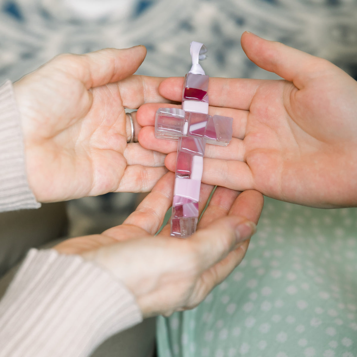 A pink mosaic cross being exchanged between two sets of hands.