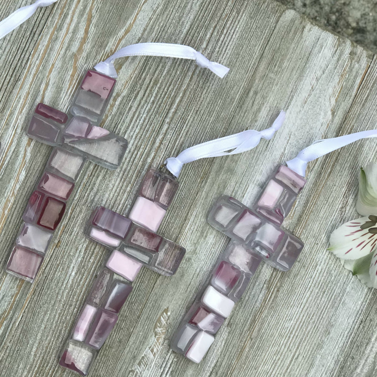 An assortment of pink mosaic crosses with varying shades of pink, white, and clear glass.